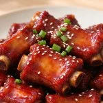 A plate of glossy sweet and sour pork ribs topped with sesame seeds and spring onion